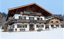 A large, rustic chalet in the snow, surrounded by a wintry landscape. The sky is clear and the surroundings are peaceful.