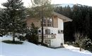 A cozy chalet in the snow with a traditional wooden balcony. The surroundings are wintry and peaceful.