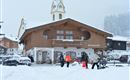 A traditional wooden house in the snow with a clock tower. People walk by and enjoy the winter landscape.