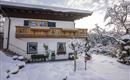 Ein winterliches Haus mit einem Balkon, umgeben von Schnee. Der Garten ist mit schneebedeckten Bäumen dekoriert.
