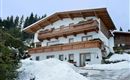 A charming holiday home in the snow with wooden balustrades and a picturesque backdrop of coniferous trees. The facade is friendly and welcoming.
