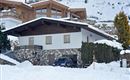 A house in the snow with a stone foundation and a modern roof. Fresh snow is everywhere, and there are some green bushes.