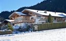 A beautiful, snow-covered building in the mountains. Surrounded by trees and a clear sky.