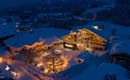 Ein malerisches Hotel in einer verschneiten Landschaft bei Nacht. Das Gebäude ist warm erleuchtet und von schneebedeckten Bäumen umgeben.