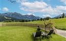 A beautiful meadow with two loungers and a view of the mountains. The sky is bright blue with some clouds.