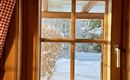 A window with a wooden frame that overlooks a snowy landscape. The gentle sun rays bathe the room in warm light.