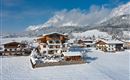 Eine malerische Winterlandschaft mit schneebedeckten Häusern und Bergen im Hintergrund. Der Himmel ist klar und blau, was die Szene besonders einladend macht.