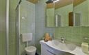 A modern bathroom with green tiles and a large mirror. The fixtures include a shower, a sink, and a toilet.