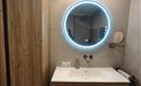 A modern bathroom with wooden cabinets and an elegant sink. An illuminated round mirror complements the stylish design.