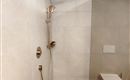 A modern bathroom with an elegant shower and golden fittings. The walls are tiled in light tones, creating a calming atmosphere.