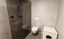 A modern bathroom with a shower, a toilet, and a washing machine. The walls are designed in light, neutral colors.