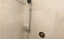 Een moderne douche met een grote regendouche en handdouche. De wanden zijn voorzien van lichte tegels.