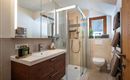 A modern bathroom with a shower and a wooden sink. Natural light falls through the window onto the bright design of the room.
