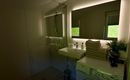 A modern bathroom with a large mirror surface and a washing machine. The ambiance is bright and friendly, with a couple of green plants.