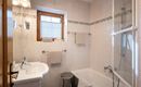 Ein modernes Badezimmer mit einer Badewanne und einer Dusche. Die Wände sind hell gefliest, und es gibt ein Fenster für natürliches Licht.