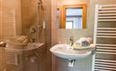 Ein modernes Badezimmer mit einer Dusche, einem Waschbecken und Handtüchern. Die Wände sind mit hellen Fliesen gefliest und es gibt einen Handtuchtrockner.