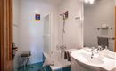 Ein modernes Badezimmer mit einer Badewanne und einer Dusche. Helle Fliesen und einige dekorative Bilder an der Wand sorgen für eine freundliche Atmosphäre.