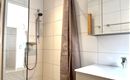 Ein modernes Badezimmer mit einer Dusche und einer großen Spiegelschranke. Die Wände sind hell gefliest und der Raum wirkt sauber und einladend.