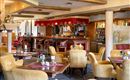 Ein elegantes Restaurant mit gemütlichen, gelben Sesseln und Holztischen. Die Bar im Hintergrund ist gut ausgestattet und lädt zum Verweilen ein.