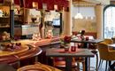 Eine gemütliche Bar mit stilvollem Interieur und roten Akzenten. Auf den Tisch stehen Kerzen und kleine Blumenarrangements.