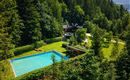 An idyllic house amidst trees with a blue swimming pool. The green space around the house invites you to relax and linger.