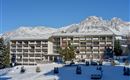 A modern building in the snow with high mountains in the background. The surroundings are wintry and clear with a blue sky.