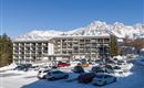 A modern hotel building in a snow-covered landscape. In the background, majestic mountains and a clear blue sky can be seen.