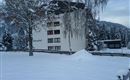 A snow-covered building with the inscription "Berghof". In the background, snow-covered trees and hills are visible.