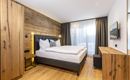 A modern bedroom with wooden paneling and a large window. It is stylishly furnished with a cozy bed and a wooden table.