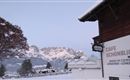 Snow-covered mountains in the background and a charming café in the foreground. The landscape is peaceful and wintry.