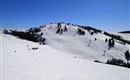 Eine verschneite Berglandschaft unter blauem Himmel. Es gibt Skilifte und sanfte Hänge für Skifahrer.