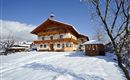 A beautiful, snow-covered house with rustic balconies. Surrounded by snow-covered trees and a clear winter landscape.