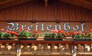 A wooden building with the inscription "Breitenhof" and colorful flower boxes. The façade radiates a cozy atmosphere.