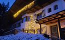 Een gezellig huis in de winter met sneeuw en feestelijke verlichting. Een kerstboom staat voor de voordeur en zorgt voor een uitnodigende sfeer.