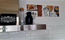 Een moderne keuken met een elegante metalen afdekking. Op het aanrecht staan een glazen karaf, een zwarte koffiecontainer en een decoratieve wandversiering met koffie- en koekjesafbeeldingen.