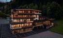 Ein modernes Gebäude mit mehreren Stockwerken, das gemütliche Apartments bietet. Die Fassade ist aus Holz und Stein, umgeben von grünen Bäumen.