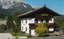 Ein traditionelles chalet mit braunem Dach und bunten Blumen. Im Hintergrund sind majestätische Berge und ein klarer blauer Himmel zu sehen.