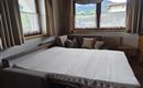 A spacious room with a sofa bed and several cushions. Large windows let in a lot of daylight and offer a view of nature.