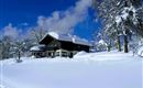 A beautiful, snow-covered house in a winter landscape. The sky is clear and blue, surrounded by snow-covered trees.