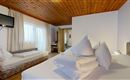 A cozy room with wooden floor and bright wooden ceiling. There is a double bed with many pillows and a single bed on the side.
