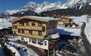 A cozy hotel in the mountains, surrounded by snow-covered landscapes. The majestic mountains rise in the background under a clear blue sky.