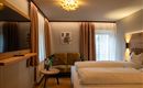 A modern room with two beds and a cozy sofa. Large windows let in plenty of light and create an inviting atmosphere.