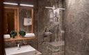 A modern bathroom with elegant marble walls and a walk-in shower. Neatly arranged towels and decorative plants are placed on the dresser.