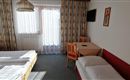 A cozy hotel room with two single beds and a table. Large windows provide plenty of daylight.