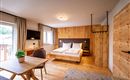 A modern room with wooden decor, a double bed, and a table. Large windows provide plenty of daylight and a cozy atmosphere.