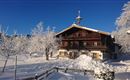A picturesque wooden house in the snow, surrounded by frosty trees. The clear blue sky complements the winter landscape.