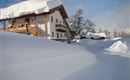 Ein verschneites Haus steht in einer winterlichen Landschaft. Der Schnee ist hoch und bedeckt die Umgebung.