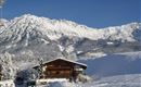 A charming wooden house in a snowy winter landscape. In the background, majestic mountains rise under a clear blue sky.