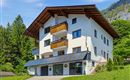 Ein modernes Haus mit Holzverzierungen und mehreren Balkonen. Es ist von Bäumen und grüner Landschaft umgeben.