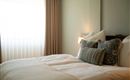 Een gezellige slaapkamer met een uitnodigend bed en zachte kussens. Het zachte licht van de ramen creëert een ontspannen sfeer.